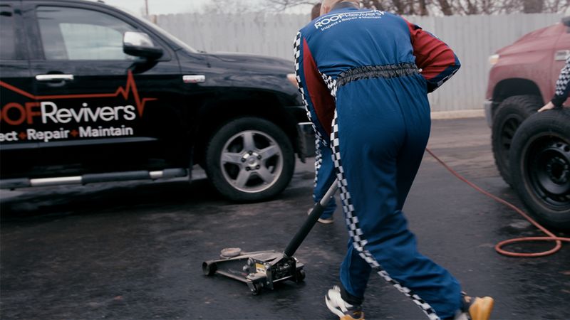 Depicts roofers in racing gear working on a roofing repair truck. 