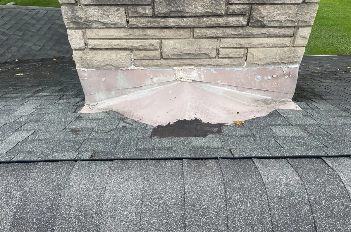 Patched metal flashing and old sealant at the base of a stone chimney on a Blacklick, Ohio roof, before repair