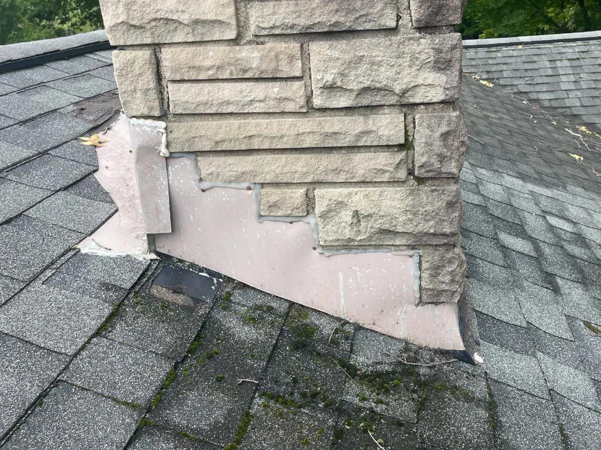Old painted side flashing and moss on the shingles beside the chimney in Blacklick, Ohio, before repair