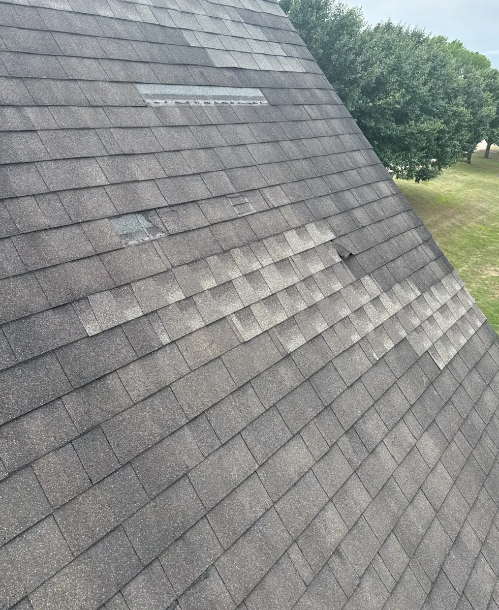 Weathered shingles with mismatched patches and a missing piece on a steep roof slope in Dunn, North Carolina, before replacement