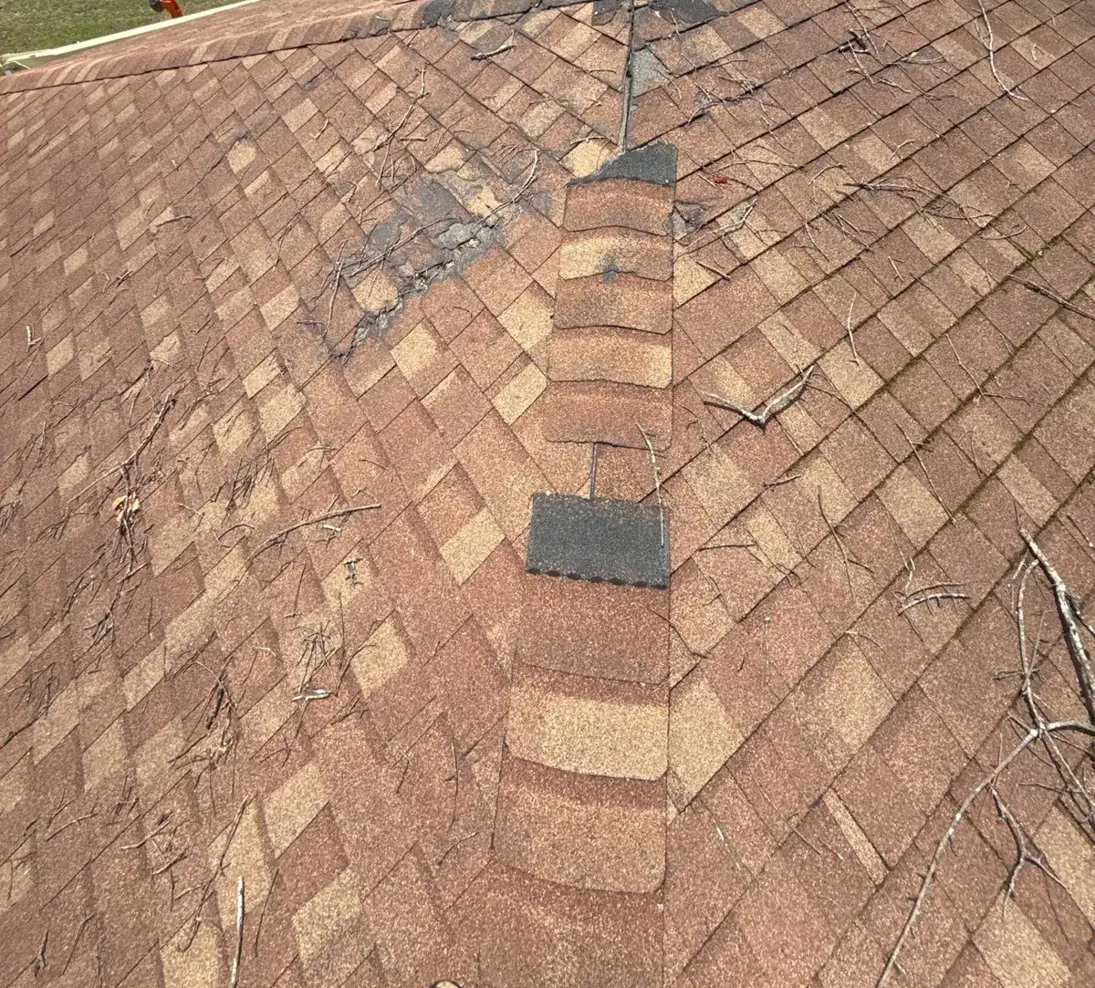 Weathered tan shingles with patched spots along the ridge on a Goldsboro, North Carolina roof, before replacement