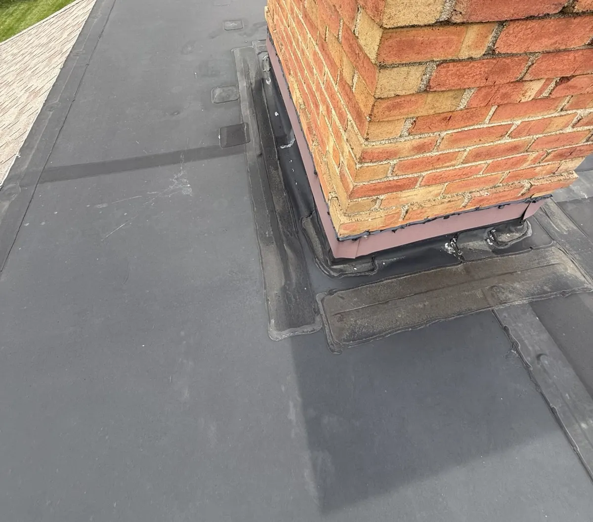 Patched rubber membrane and tar-sealed flashing around the chimney base on the flat roof in New Albany, Ohio, before repair