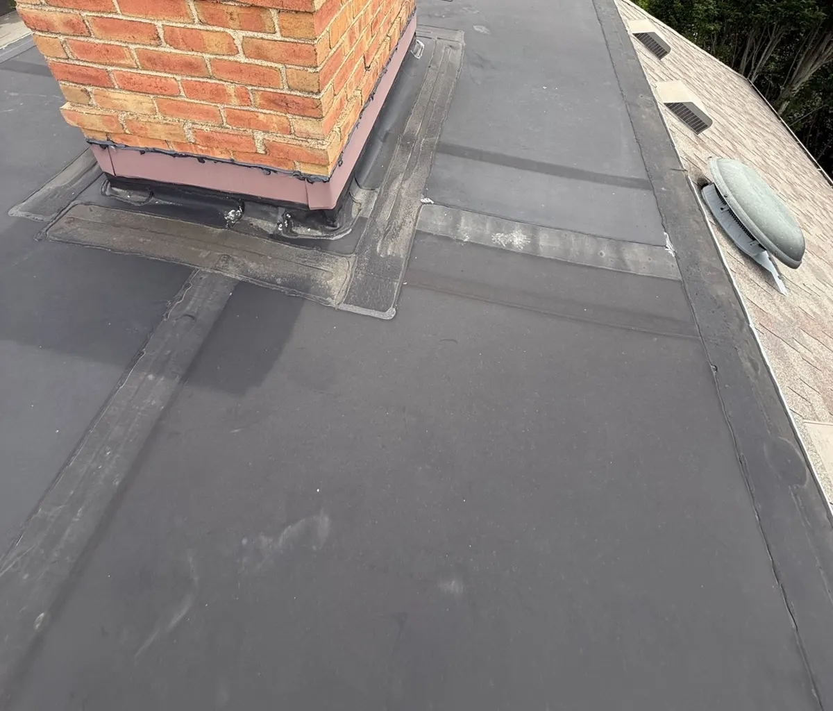 Worn rubber flat roof section with patched seams and old flashing at the brick chimney on a New Albany, Ohio home, before repair