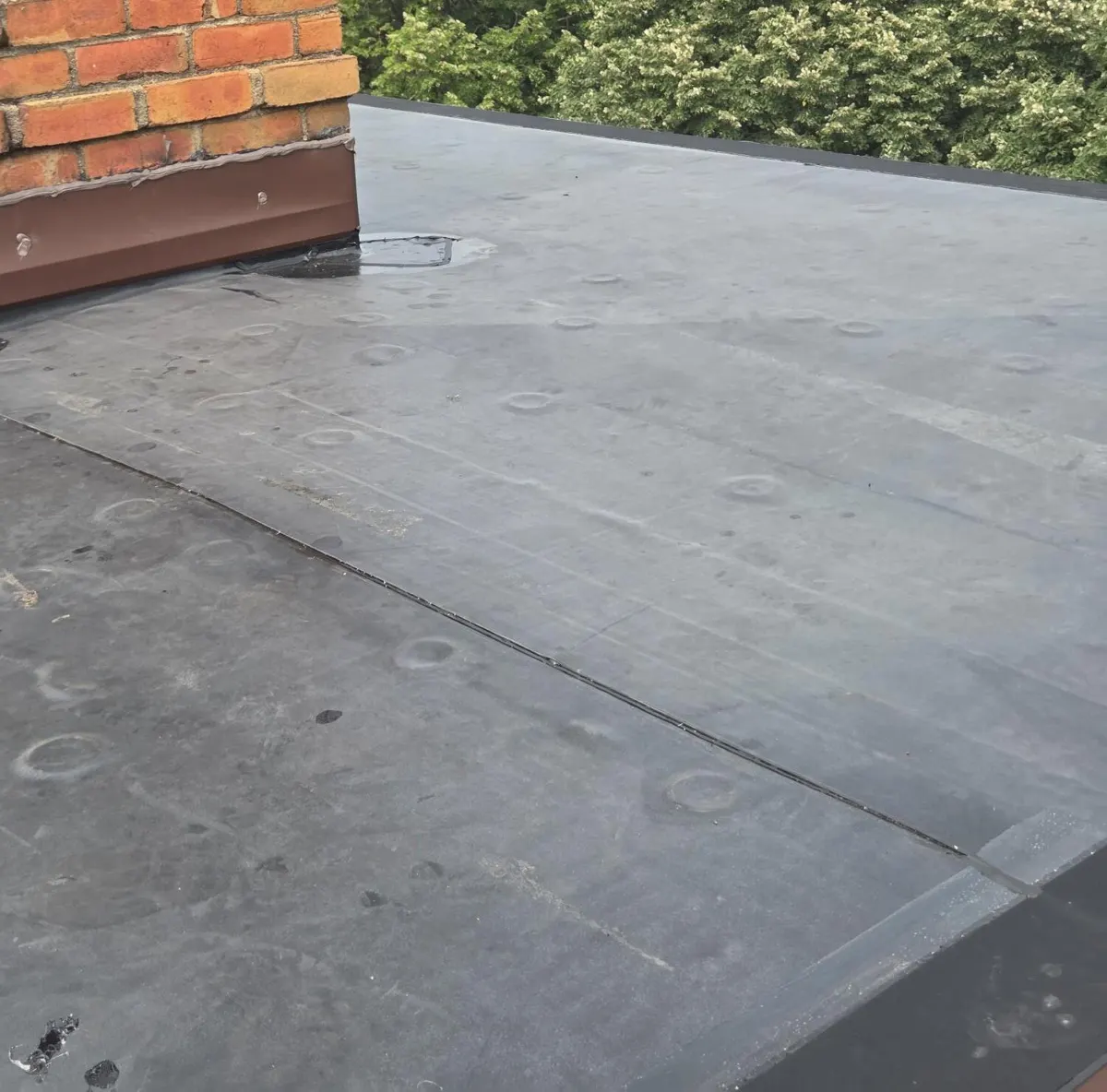 New EPDM rubber membrane meeting the chimney with new brown metal flashing in New Albany, Ohio, after repair